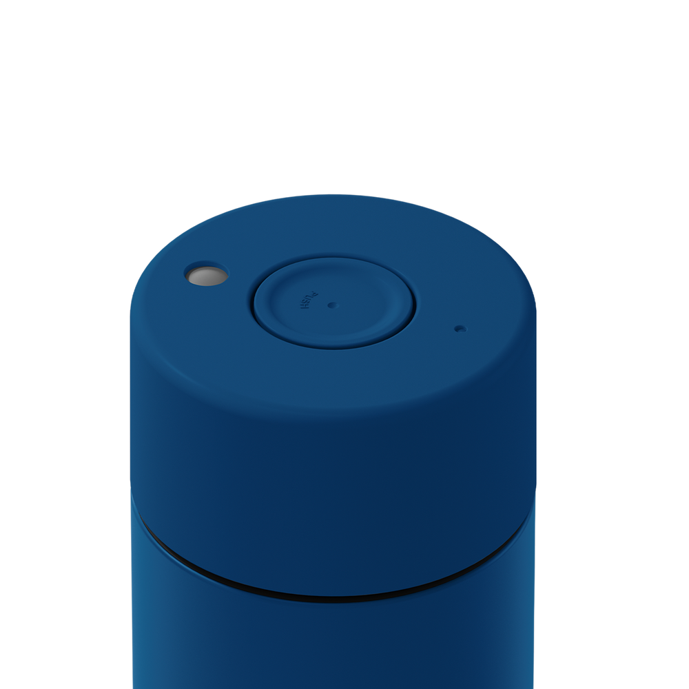 Close-up of the top of a blue cylindrical container or device with a circular button, a small light, and a small port on a white background.