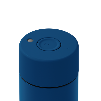 Close-up of the top of a blue cylindrical container or device with a circular button, a small light, and a small port on a white background.