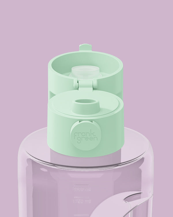 A mint green water bottle lid with a flip-top spout and a circular 'frank's green' logo, shown on top of a translucent lavender water bottle against a solid lavender background.