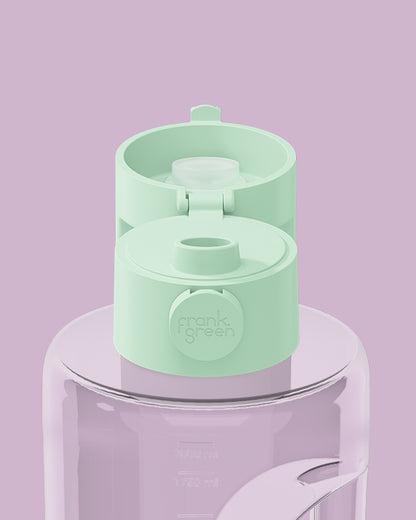 A mint green water bottle lid with a flip-top spout and a circular 'frank's green' logo, shown on top of a translucent lavender water bottle against a solid lavender background.
