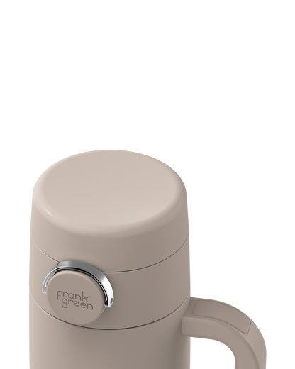 Close-up of a beige insulated bottle lid with a silver ring and the 'frank green' logo, on a white background.
