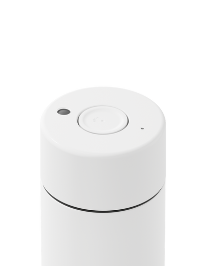 A close-up of a white cylindrical device, likely a portable coffee maker or similar appliance, showing the top lid with a central button and small sensor details, isolated on a white background.