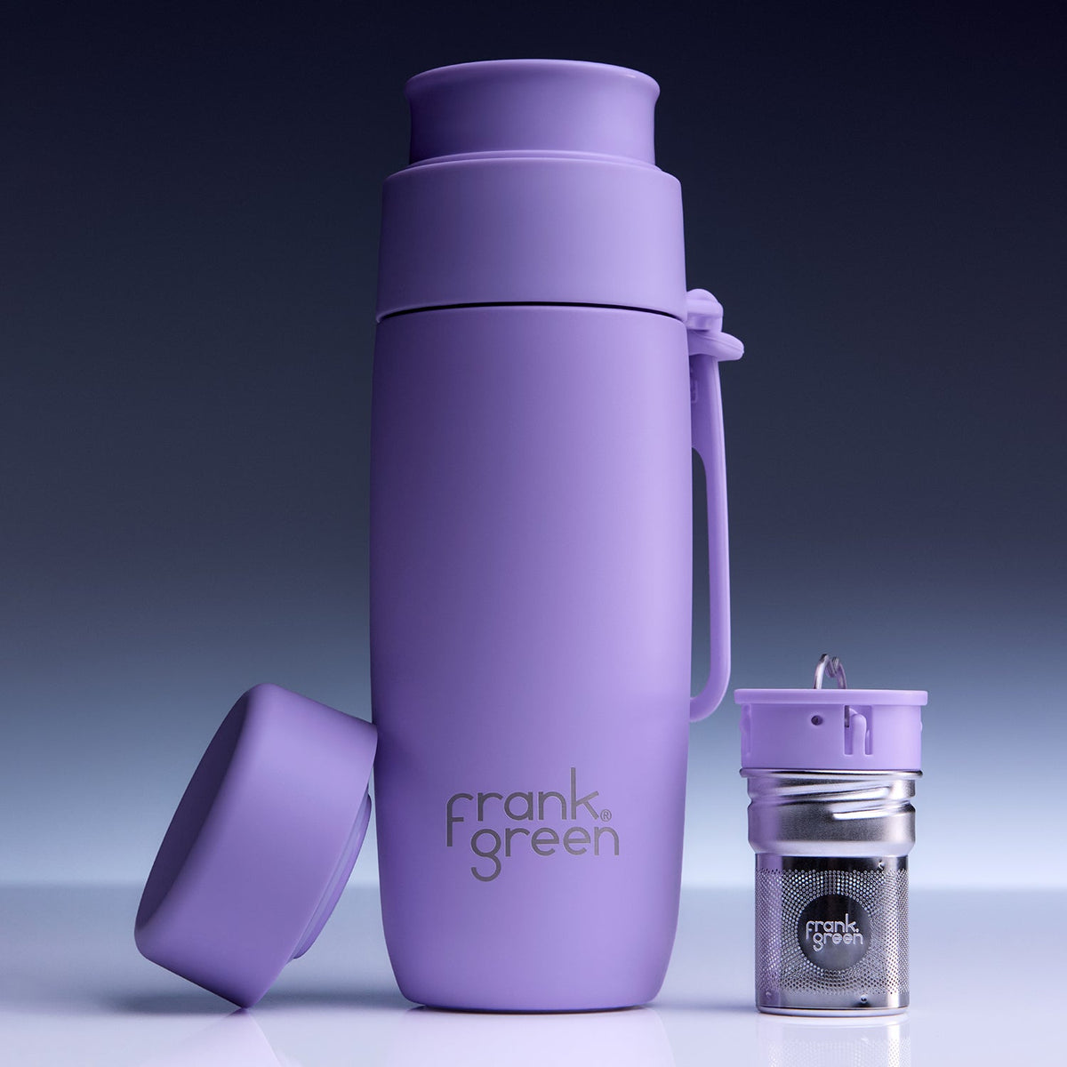 A purple Frank Green vacuum-insulated bottle with its lid off, shown next to a small matching purple and silver tea infuser on a clean studio background.